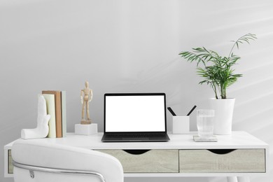 Stylish workplace with laptop, houseplant and stationery on wooden table near white wall