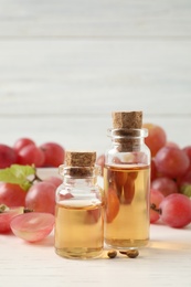 Organic red grapes, seeds and bottles of natural essential oil on white wooden table