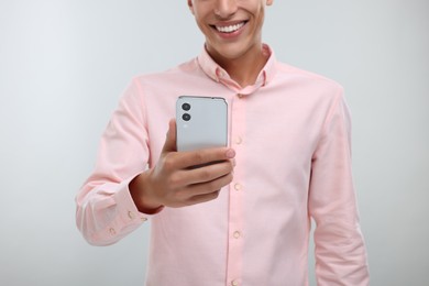 Photo of Young man sending message via smartphone on light grey background, closeup