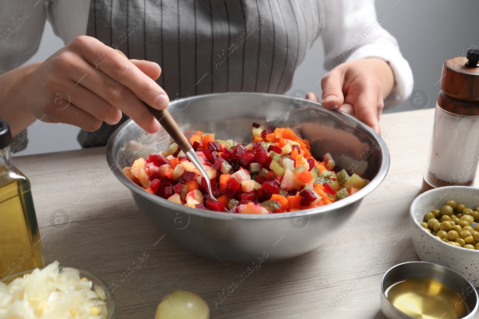 Photo of Woman preparing tasty vinaigrette salad at light wooden table, closeup