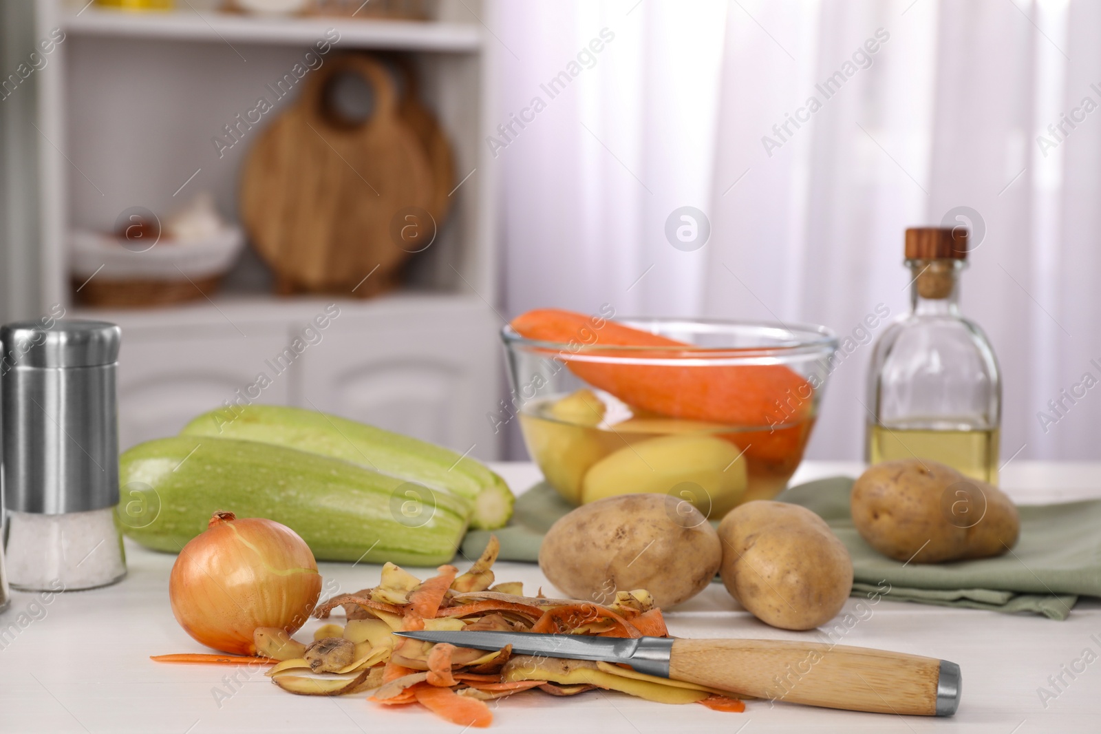 Photo of Peels of fresh vegetables and knife on white table