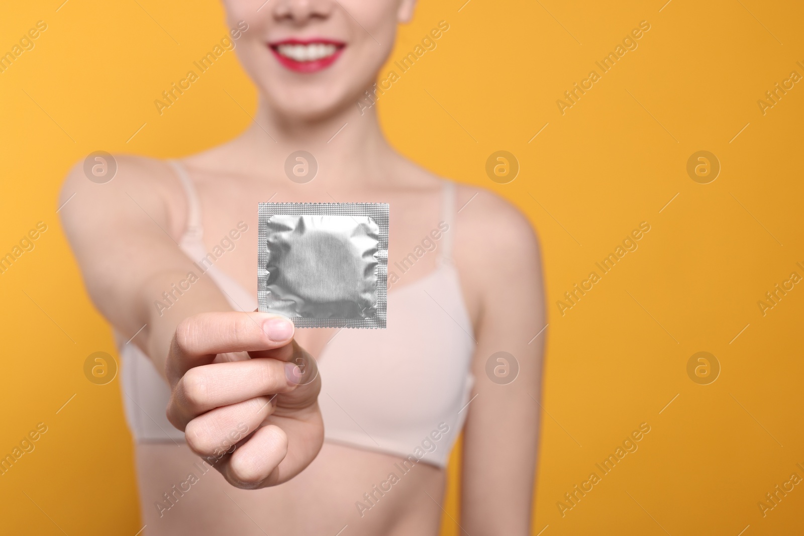 Photo of Woman holding condom on yellow background, closeup and space for text. Safe sex