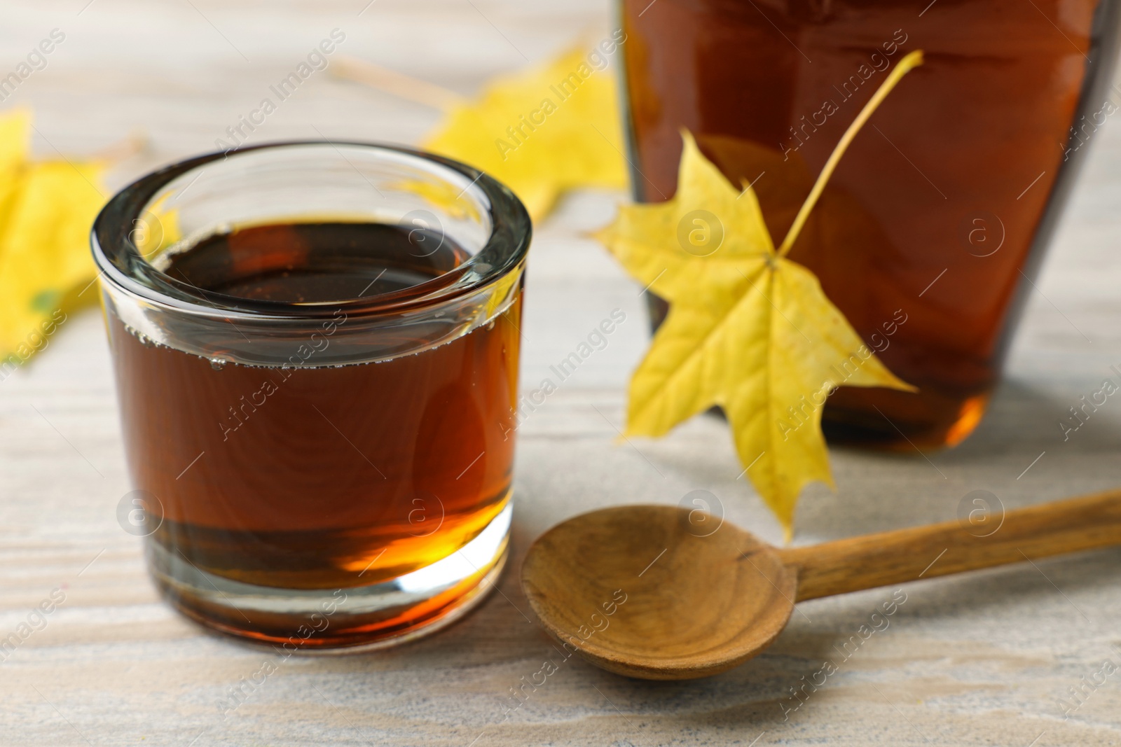 Photo of Tasty maple syrup, spoon and leaves on wooden table, closeup