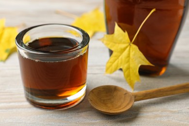 Photo of Tasty maple syrup, spoon and leaves on wooden table, closeup