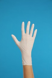 Photo of Doctor wearing medical gloves on light blue background, closeup