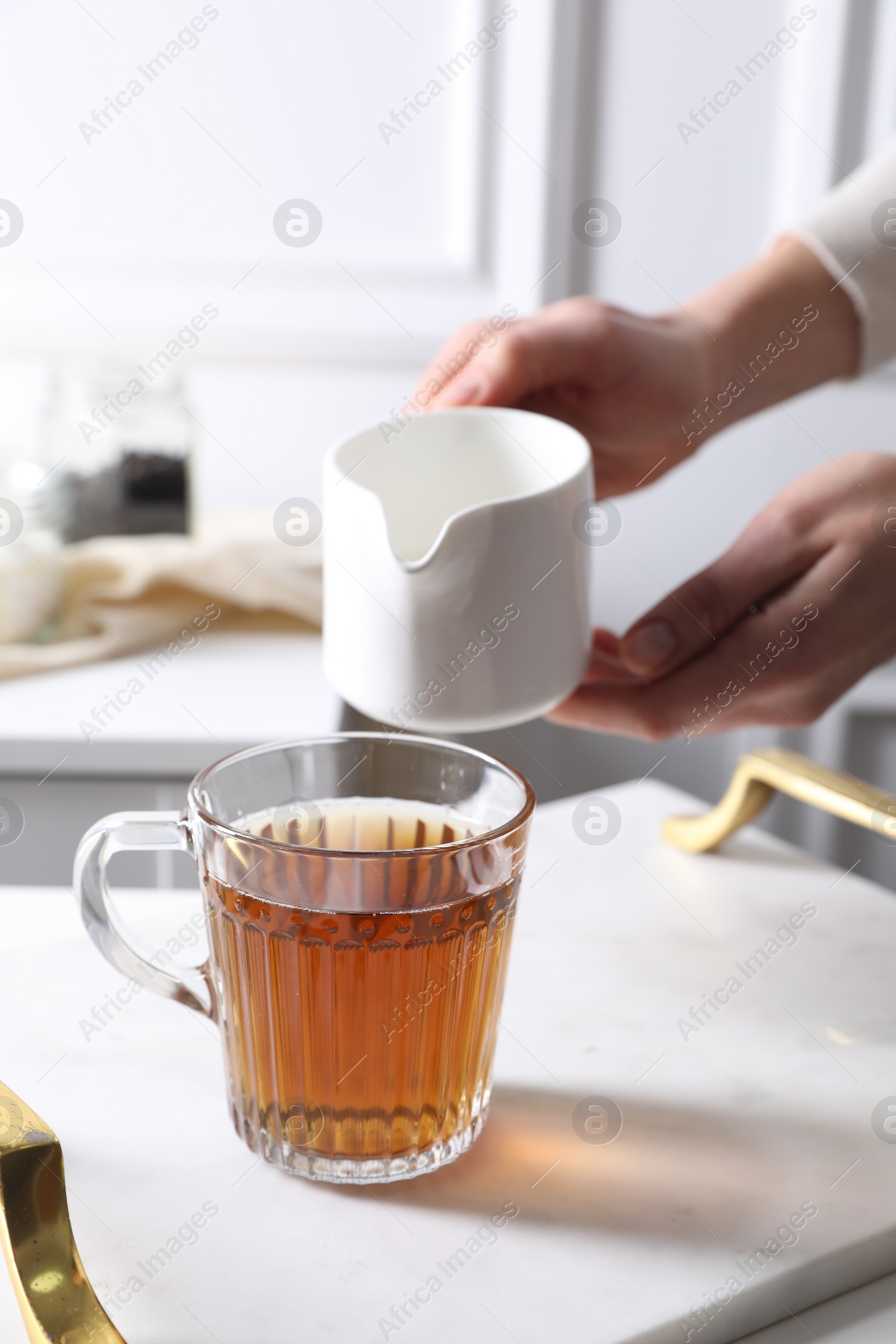 Photo of Woman pouring milk into cup of tea at white table, closeup