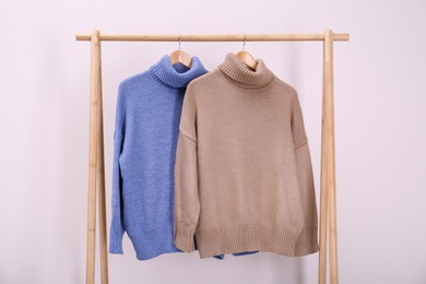 Stylish knitted sweaters hanging on clothing rack near pink wall