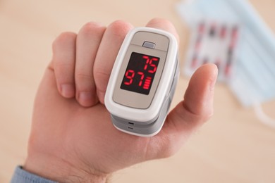 Photo of Man measuring oxygen level with modern fingertip pulse oximeter on blurred background, closeup