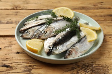 Photo of Fresh raw sprats, lemon and dill on wooden table, closeup