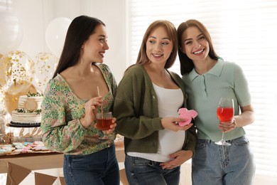 Photo of Happy pregnant woman with her friends holding tasty cookie and drinks at baby shower party