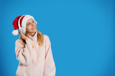 Happy woman with headphones on blue background, space for text. Christmas music