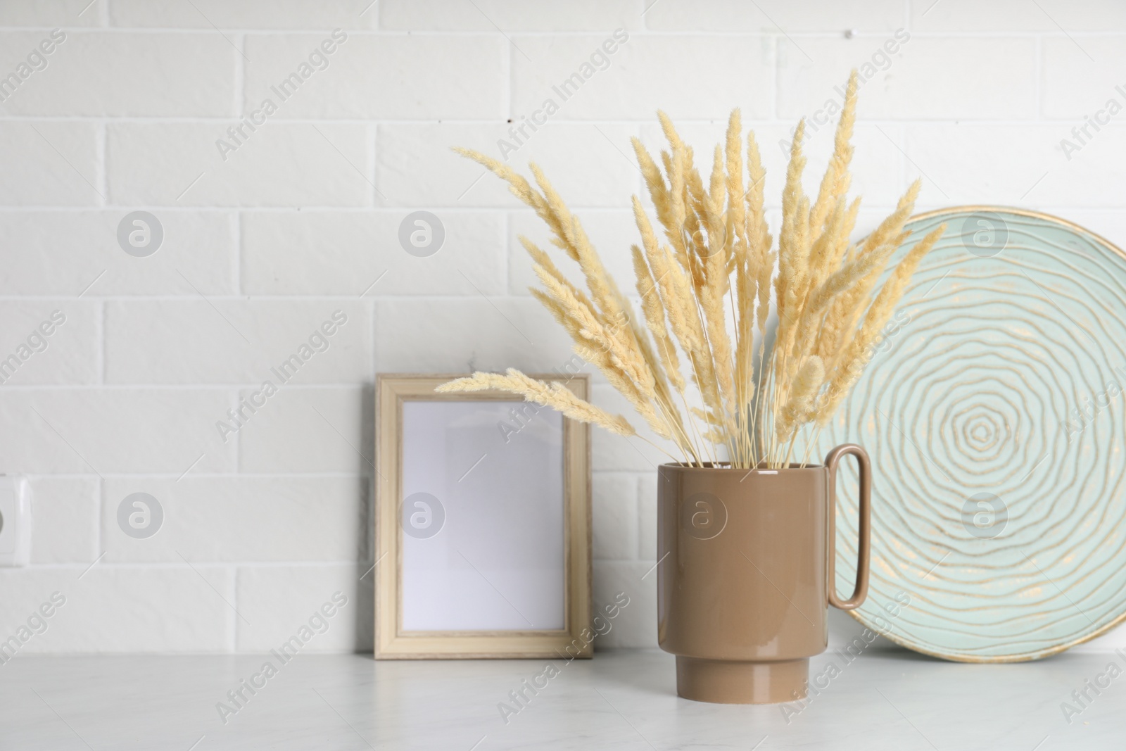 Photo of Ceramic vase with fluffy dry plants and decor on light table near white brick wall. Space for text