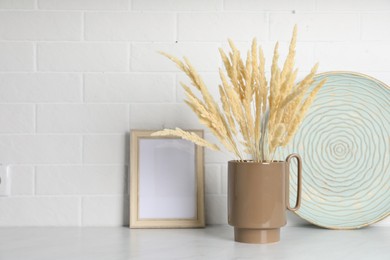 Ceramic vase with fluffy dry plants and decor on light table near white brick wall. Space for text