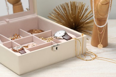Photo of Jewelry box with many different accessories and mannequin hand on white wooden table, closeup