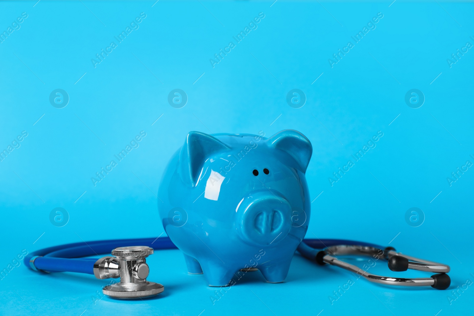 Photo of Ceramic piggy bank and stethoscope on light blue background. Medical insurance