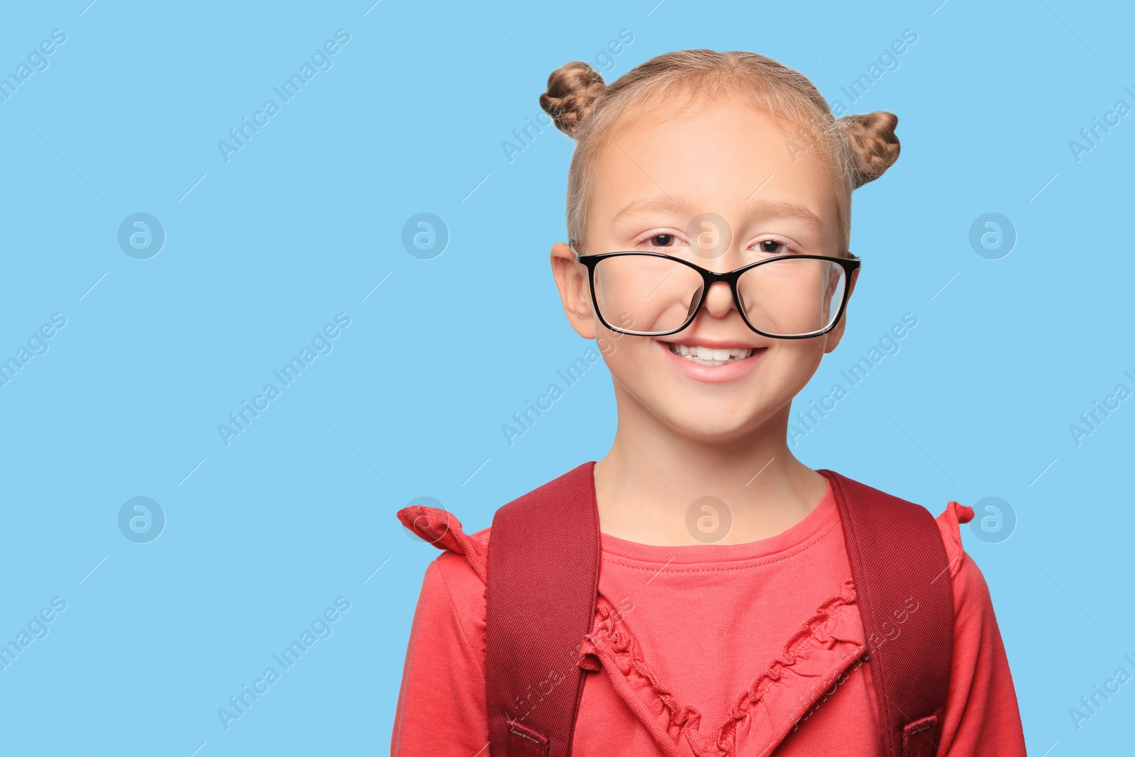 Photo of Cute little girl in glasses with backpack on light blue background. Space for text