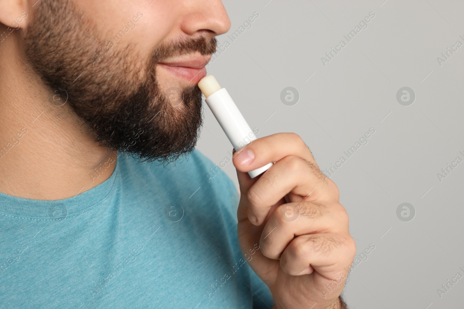 Photo of Young man applying lip balm on grey background, closeup