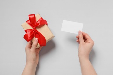 Woman holding gift box and blank card on white background, top view. Space for text