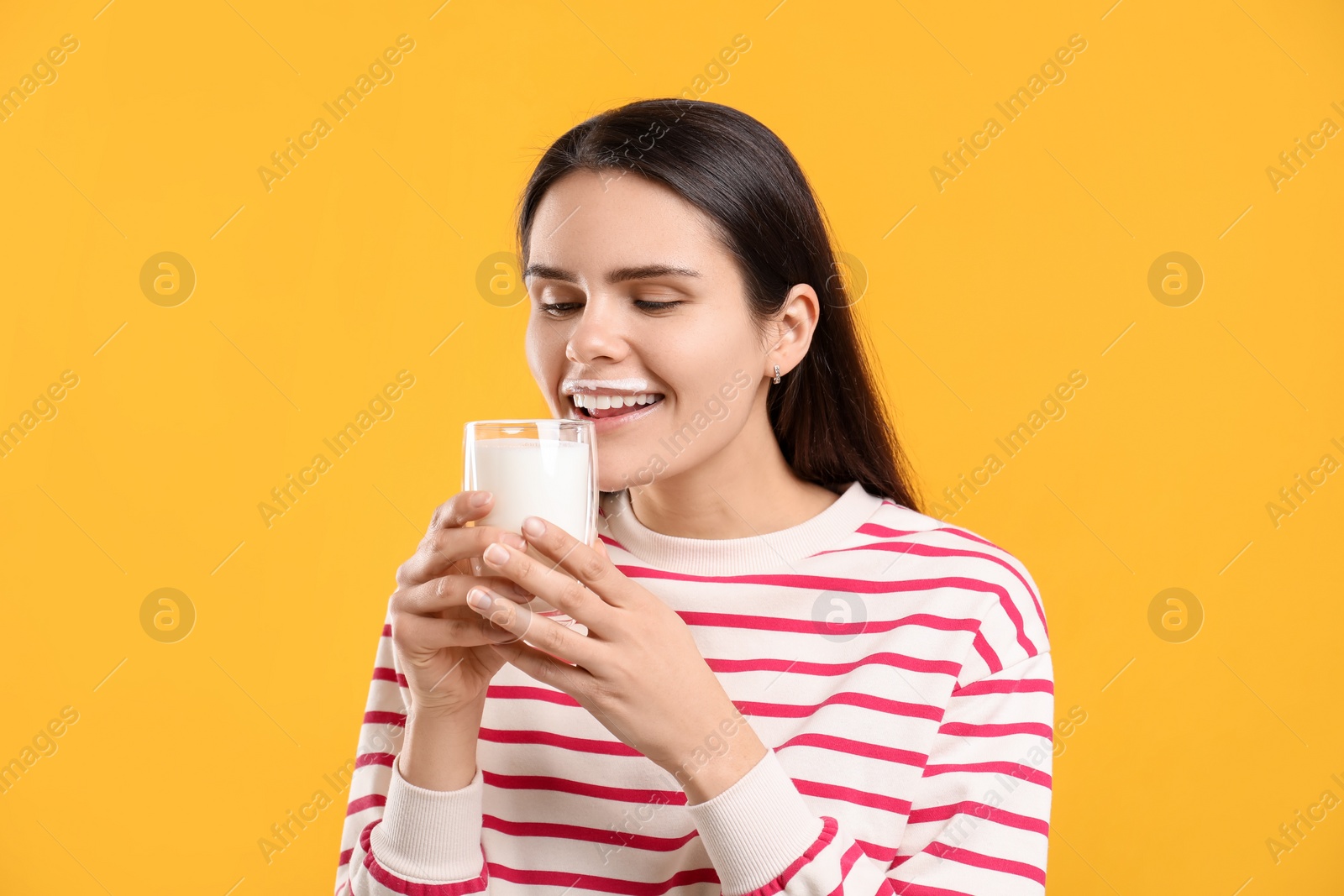 Photo of Happy woman with milk mustache holding glass of tasty dairy drink on yellow background