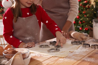 Photo of Mother and her daughter making delicious Christmas cookies at wooden table indoors, closeup