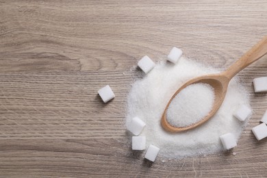 Photo of Different types of white sugar and spoon on wooden table, top view. Space for text