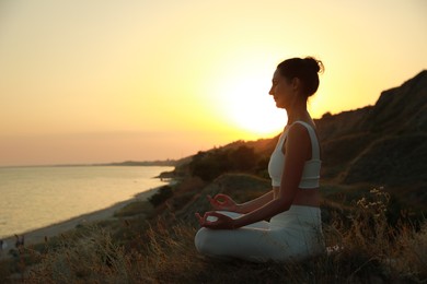 Photo of Mature woman meditating on hill near sea at sunset. Space for text