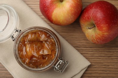 Photo of Tasty apple jam in glass jar and fresh fruits on wooden table, flat lay