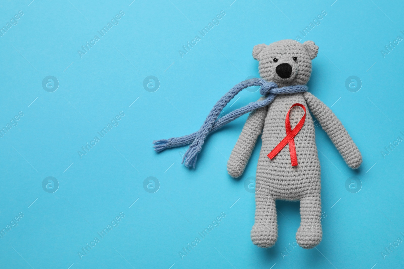 Photo of Cute knitted toy bear with red ribbon on blue background, top view and space for text. AIDS disease awareness