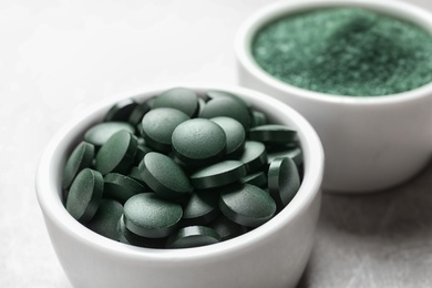 Photo of Bowls of spirulina pills and powder on color background, closeup