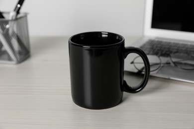 Photo of Black ceramic mug, laptop and glasses on white wooden table at workspace