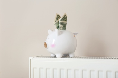 Piggy bank with money on heating radiator against light background