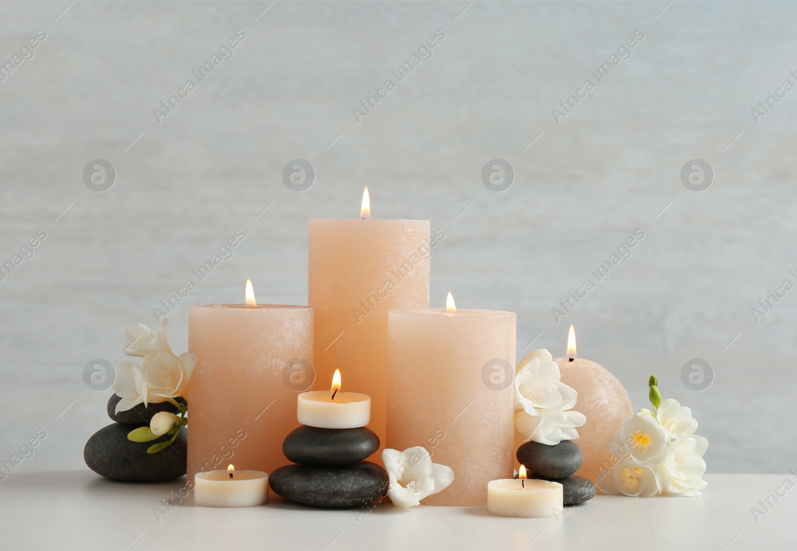 Photo of Beautiful composition with candles, stones and flowers on table against light background