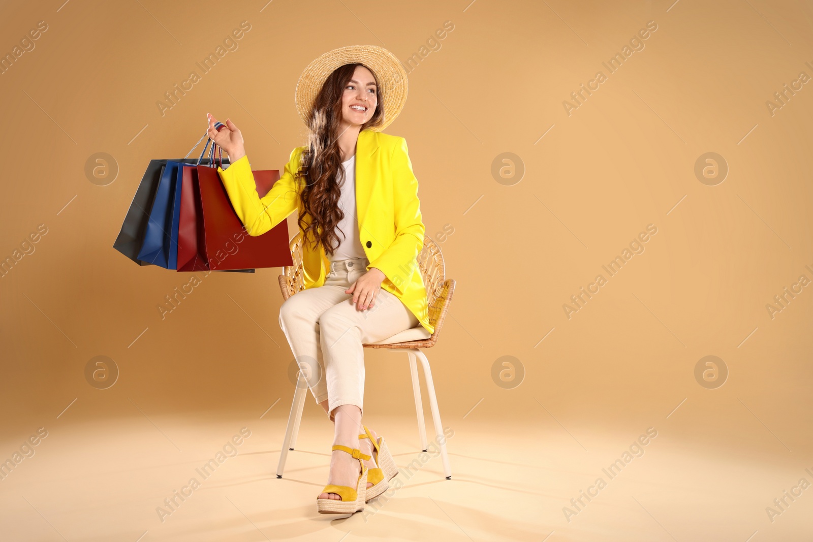 Photo of Happy woman holding many colorful shopping bags on armchair against beige background