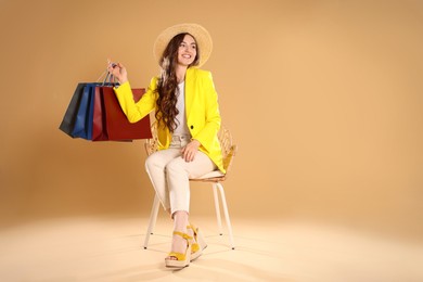 Happy woman holding many colorful shopping bags on armchair against beige background