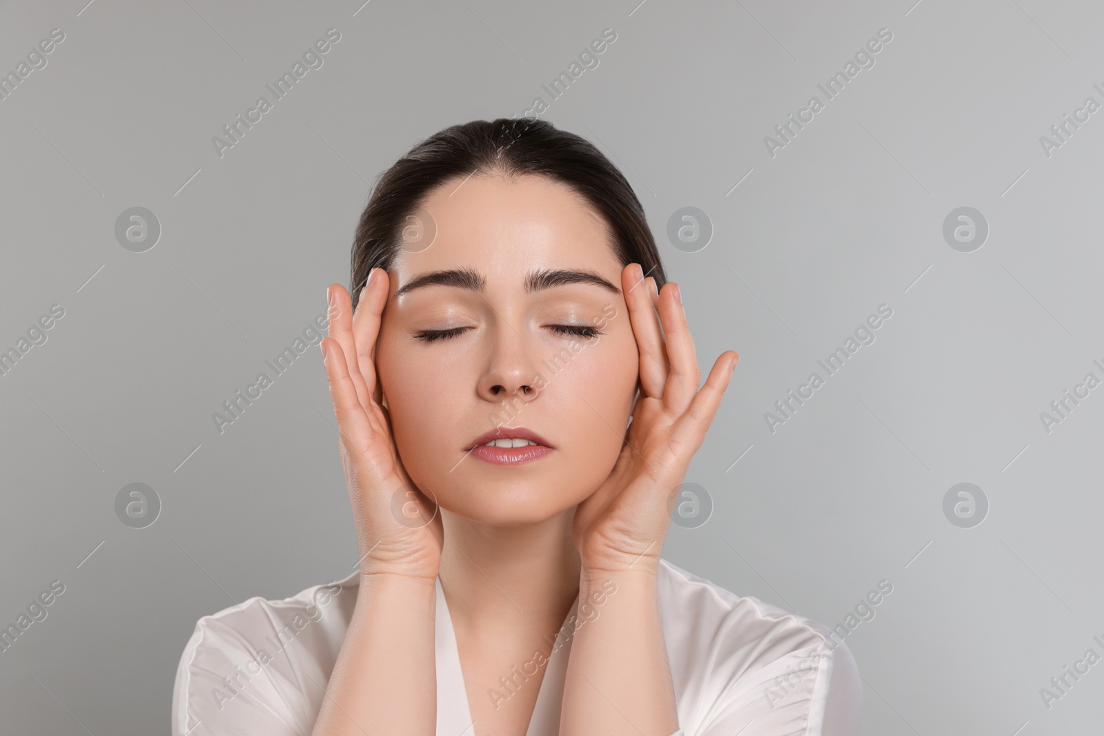 Photo of Young woman massaging her face on grey background