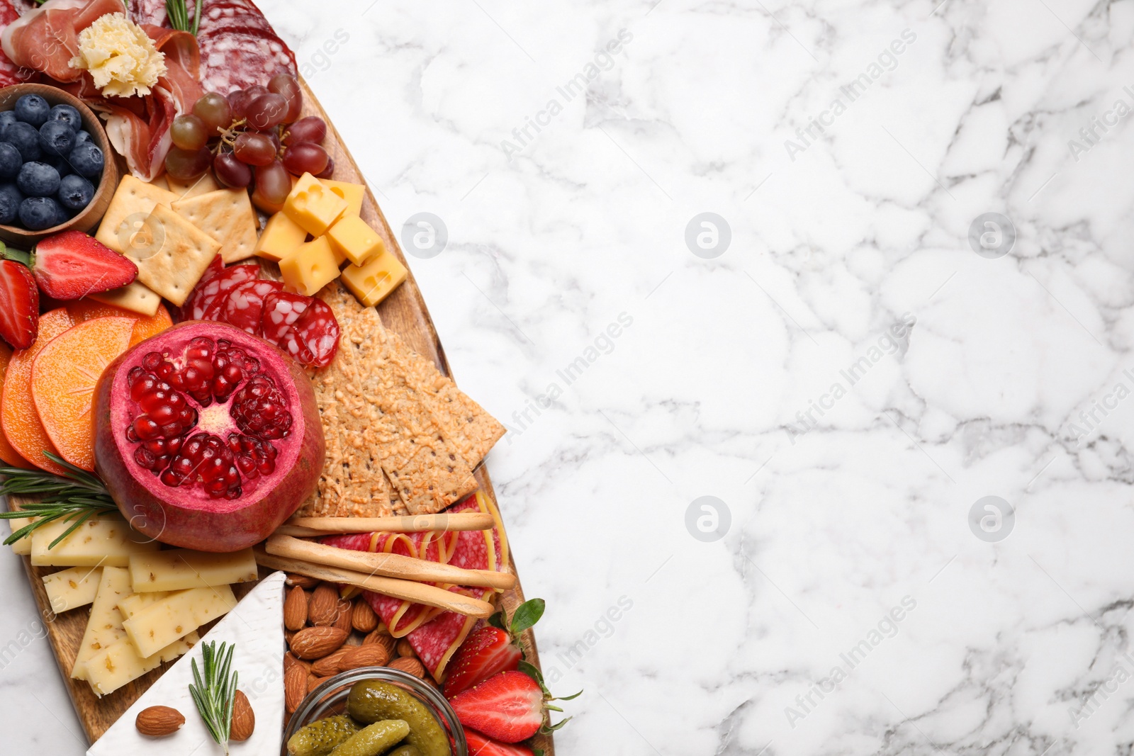 Photo of Wooden plate with different delicious snacks on white marble table, top view. Space for text