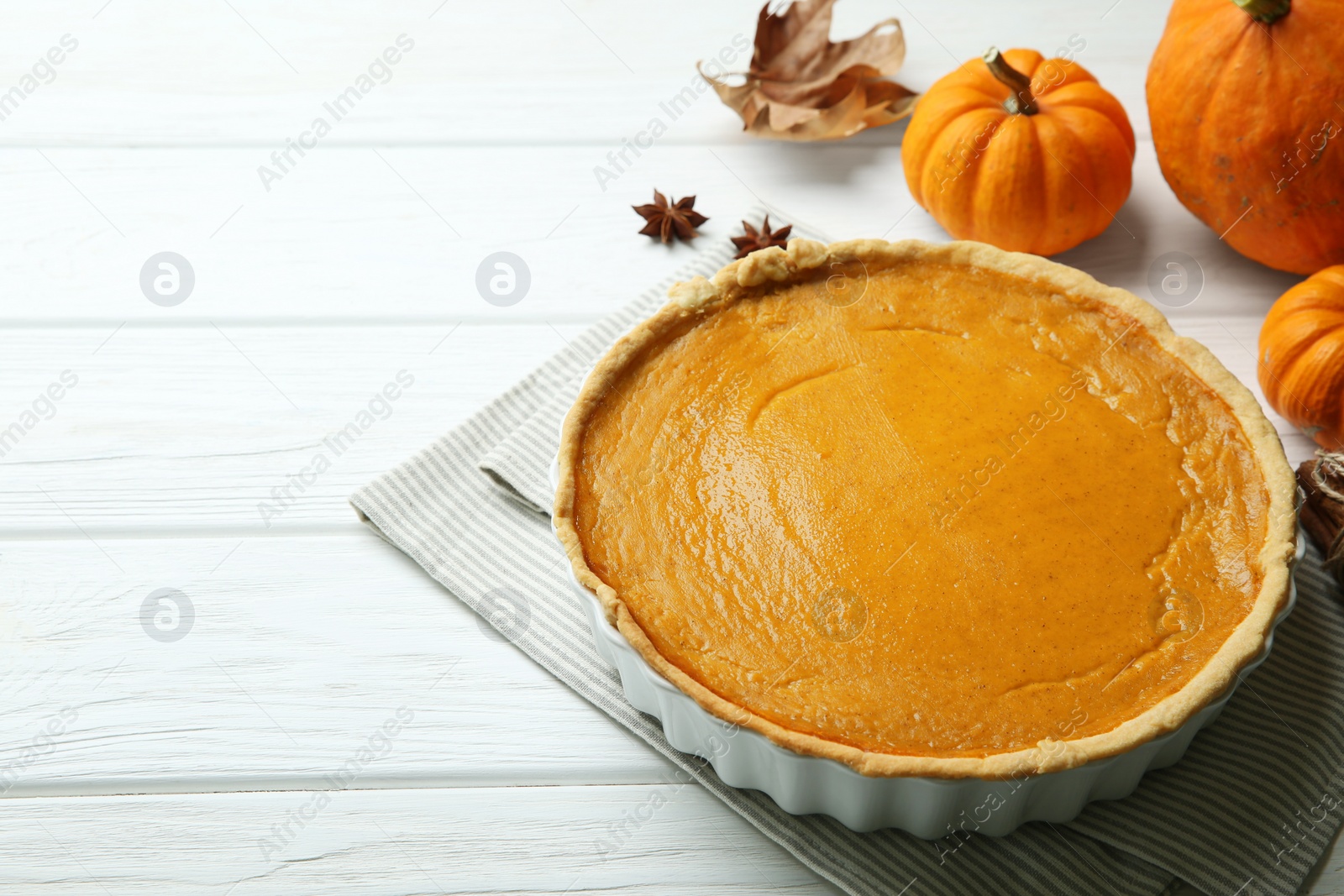 Photo of Delicious pumpkin pie and ingredients on white wooden table. Space for text