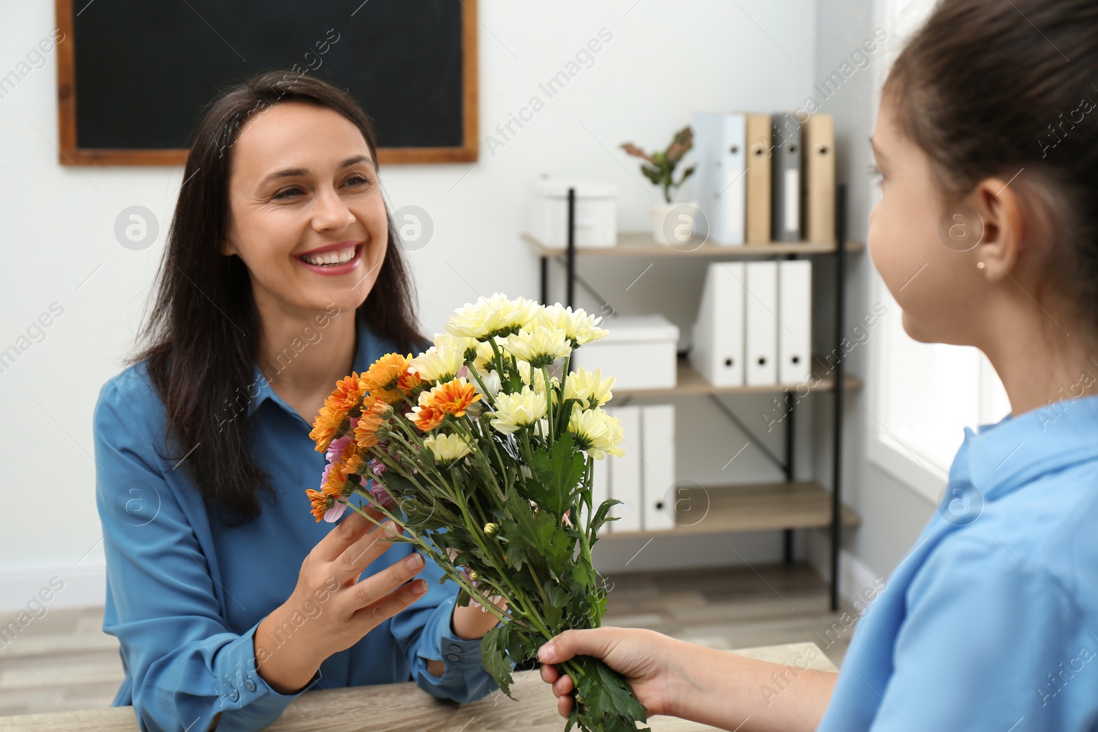 Photo of Schoolgirl congratulating her pedagogue with bouquet in classroom. Teacher's day