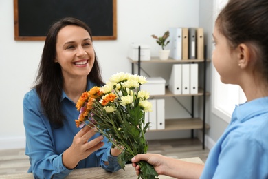 Schoolgirl congratulating her pedagogue with bouquet in classroom. Teacher's day