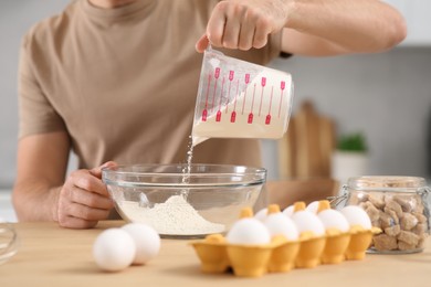 Man pouring flour into bowl at table in kitchen, closeup. Online cooking course