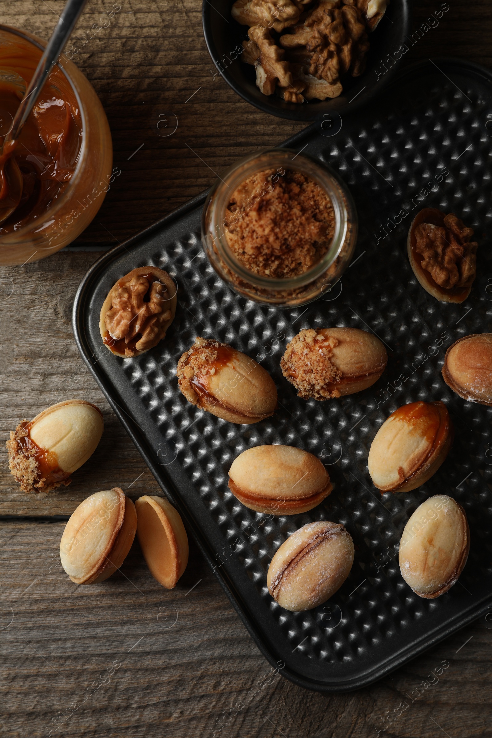 Photo of Freshly baked homemade walnut shaped cookies, boiled condensed milk and nuts on wooden table, flat lay