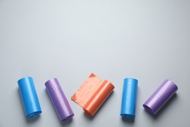 Photo of Rolls of different color garbage bags on light background, flat lay. Space for text