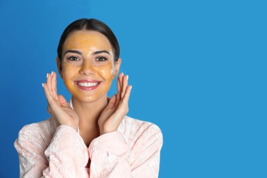 Photo of Young woman with cleansing mask on her face against color background, space for text. Skin care