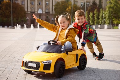 Photo of Cute boy pushing children's car with little girl outdoors on sunny day