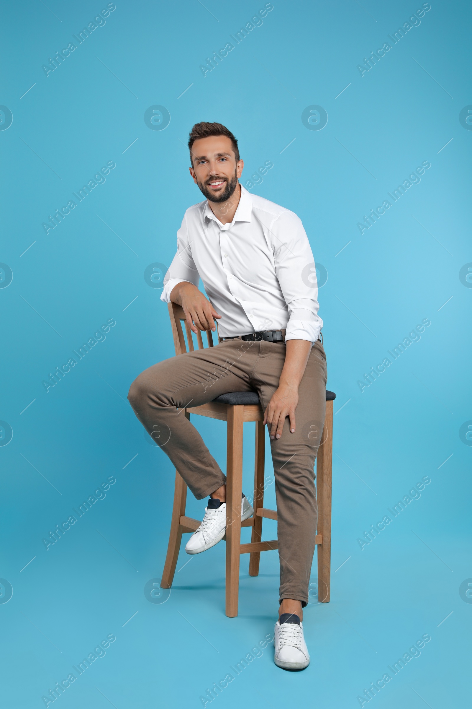 Photo of Handsome man sitting on stool against turquoise background
