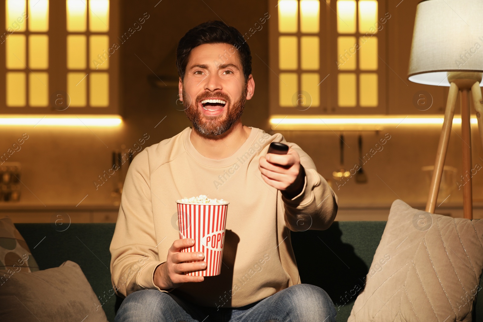 Photo of Happy man watching TV with popcorn on sofa at home