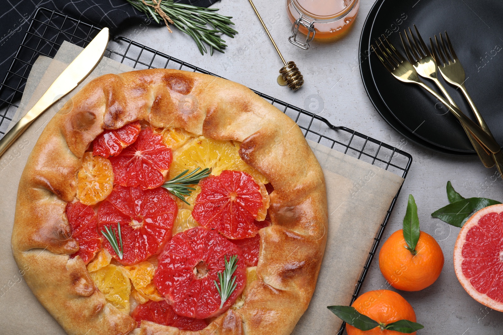 Photo of Tasty galette with citrus fruits and rosemary served on grey table, flat lay