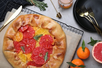 Photo of Tasty galette with citrus fruits and rosemary served on grey table, flat lay