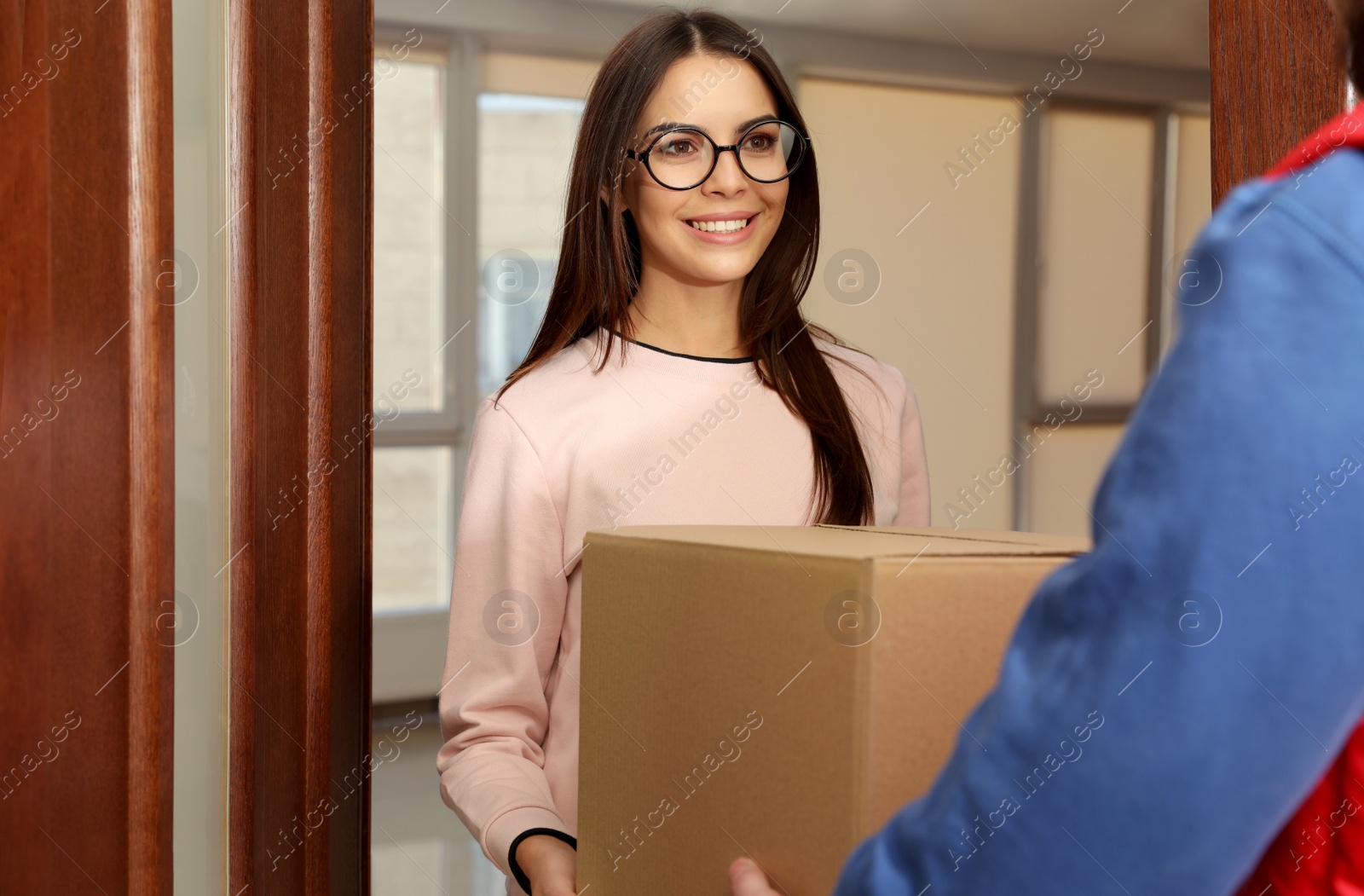 Photo of Woman receiving parcel from delivery service courier indoors