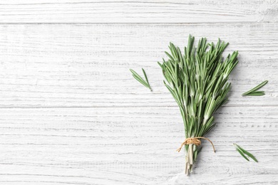 Photo of Fresh rosemary twigs tied with twine on wooden table, top view